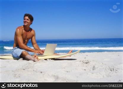 Young man sitting on a surfboard with a laptop