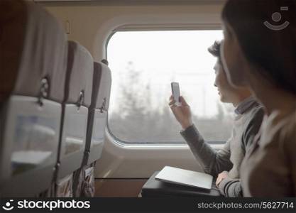 Young man sitting on a train taking a photo out the window