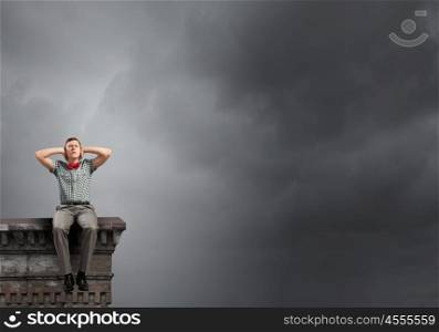 Young man sitting on building top and covering ears with hands