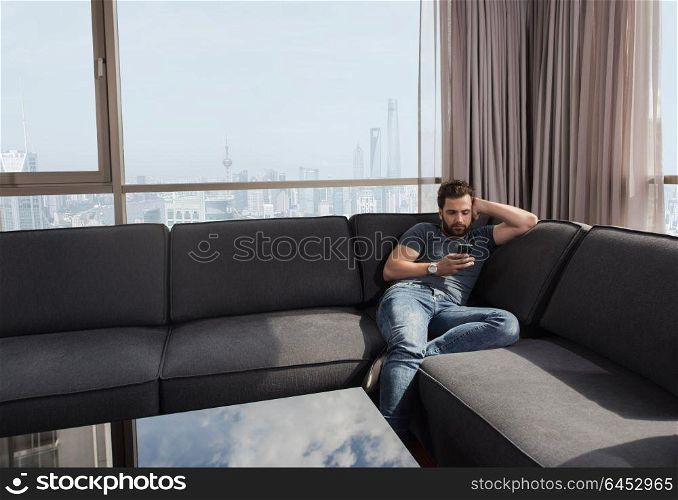 young man sitting on sofa and using a mobile phone near the window at home