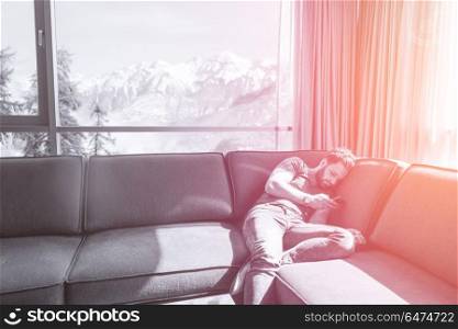 young man sitting on sofa and using a mobile phone near the window at home. young casual man using a mobile phone at home