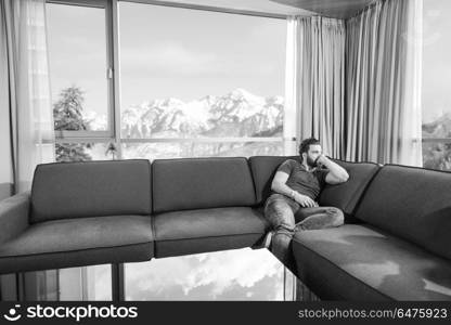 young man sitting on sofa and using a mobile phone near the window at home. young casual man using a mobile phone at home