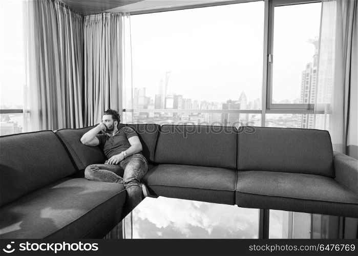 young man sitting on sofa and using a mobile phone near the window at home. young casual man using a mobile phone at home