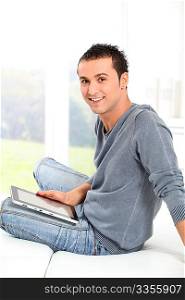 Young man sitting on sofa with electronic pad