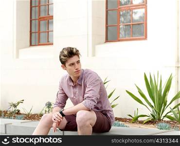 Young man sitting on step, outdoors, looking away