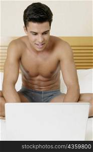 Young man sitting on the bed and using a laptop