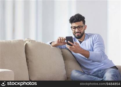 Young man sitting on the couch and using his mobile. 