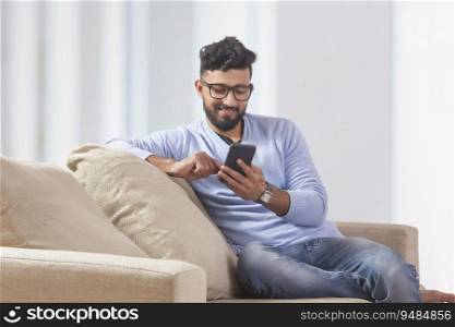 Young man sitting on the couch and using his mobile. 