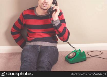 Young man sitting on the floor is on the telephone