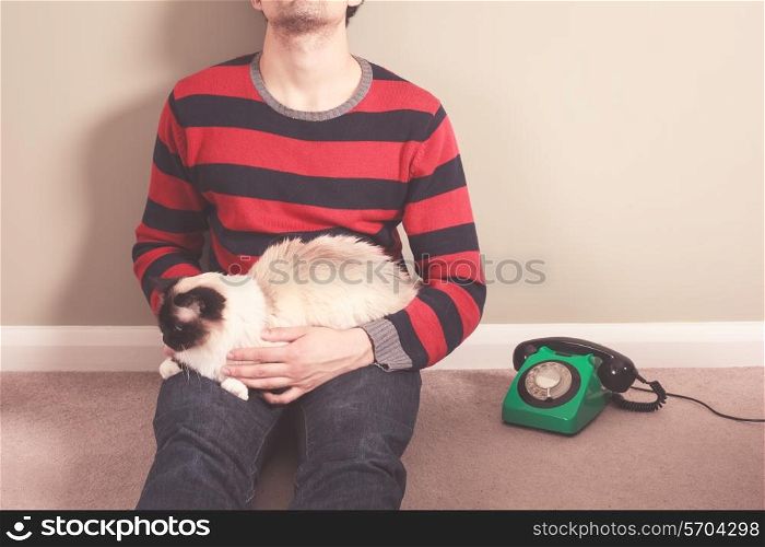 Young man sitting on the floor with his cat and telephone