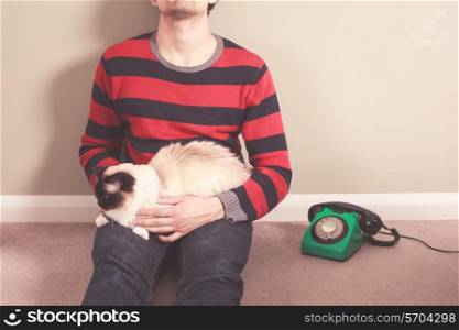 Young man sitting on the floor with his cat and telephone
