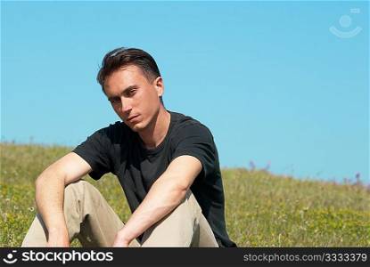Young man sitting on the grass field with blue sky