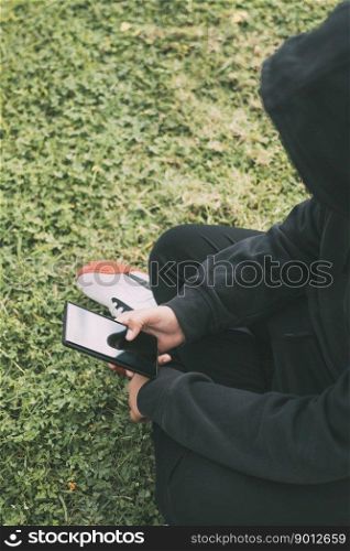 young man sitting on the ground in the park, completely immersed in his smartphone. he appears to be in his own little world, scrolling through his phone&rsquo;s contents.. young man sitting on the ground in the park, completely immersed in his smartphone.