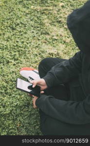 young man sitting on the ground in the park, completely immersed in his smartphone. he appears to be in his own little world, scrolling through his phone&rsquo;s contents.. young man sitting on the ground in the park, completely immersed in his smartphone.