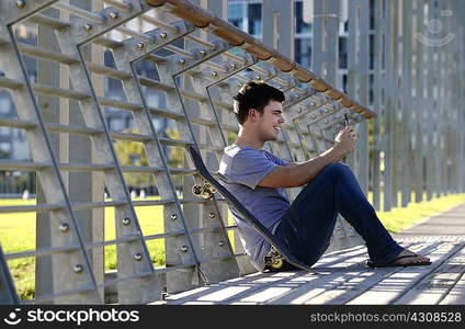 Young man sitting, using mobile phone, skateboard beside him