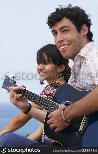 Young man sitting with a young woman and playing a guitar