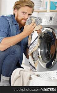 young man smelling clothes while doing laundry