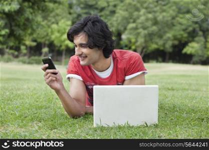 Young man smiling at mobile phone with laptop in front