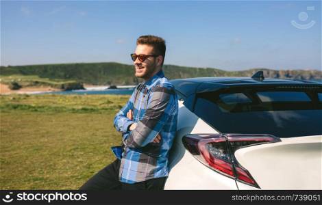 Young man smiling leaning on his car near the coast. young man leaning on his car