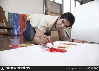 Young man smiling while painting on a large canvas at an art studio