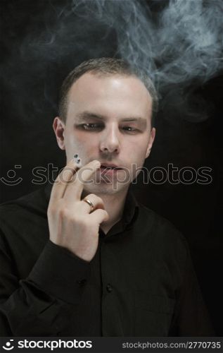 young man smokes a cigarette on a dark background