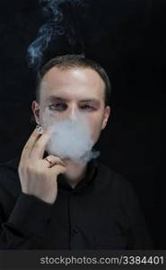 young man smokes a cigarette on a dark background