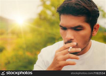 Young man smoking cigarette in the outdoors and nature background.