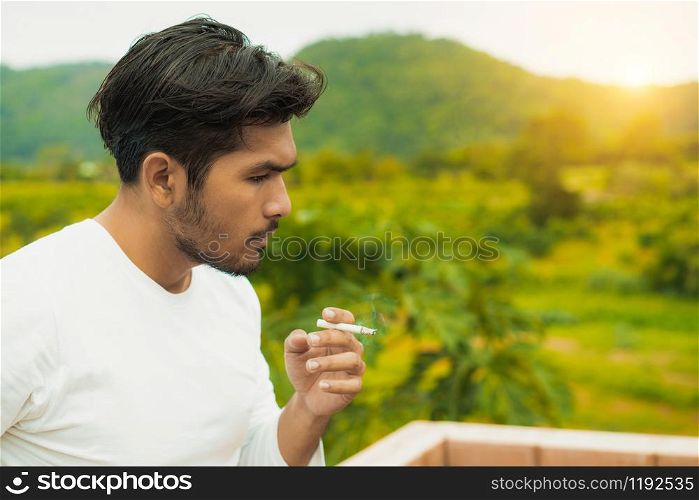 Young man smoking cigarette in the outdoors and nature background.
