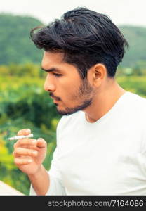 Young man smoking cigarette in the outdoors and nature background.