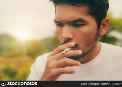 Young man smoking cigarette in the outdoors and nature background. Selective focus at cigarette.