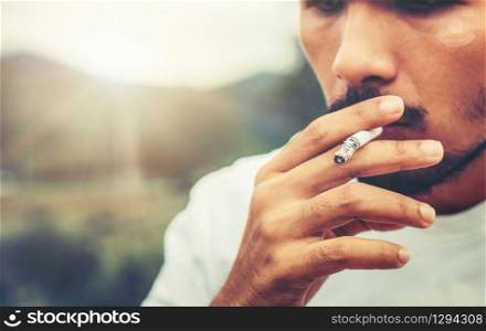 Young man smoking cigarette in the outdoors and nature background. Selective focus at cigarette.