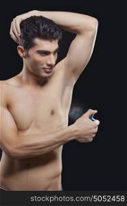 Young man spraying perfume on underarms