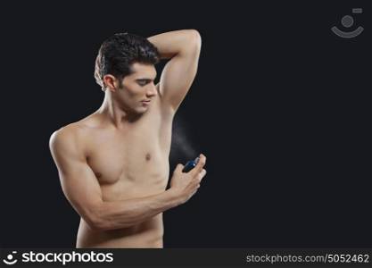 Young man spraying perfume on underarms