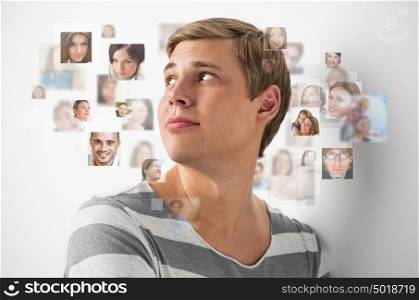 Young man standing and smiling with many different people's faces around him. Technology social media network of friends and communication.