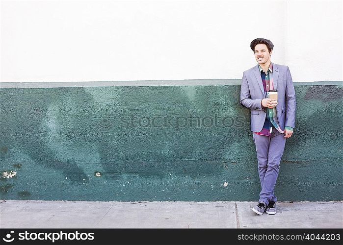 Young man standing by wall with coffee