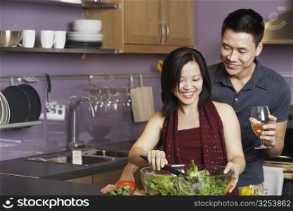 Young man standing holding a wineglass with a young woman preparing food