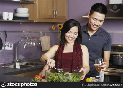 Young man standing holding a wineglass with a young woman preparing food