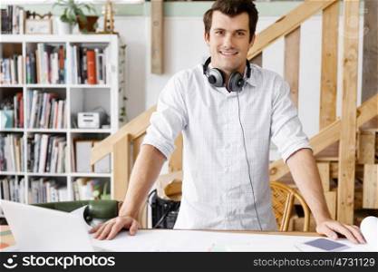 Young man standing in creative office. Smiling young designer standing in creative office in front of his desk