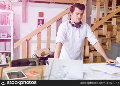 Young man standing in creative office. Smiling young designer standing in creative office in front of his desk
