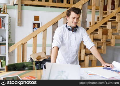 Young man standing in creative office. Smiling young designer standing in creative office in front of his desk