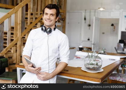 Young man standing in creative office. Smiling young designer standing in creative office in front of his desk