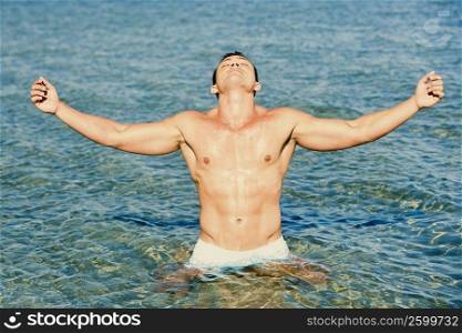 Young man standing in water with his arms outstretched