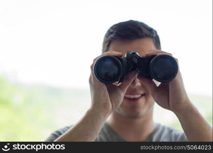 Young man standing looking through a glass window with binoculars as he watches something in the distance