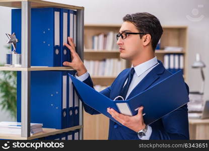 Young man standing next to the shelf with folders