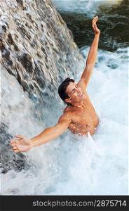Young man standing under waterfall with arms outstretched, high angle view