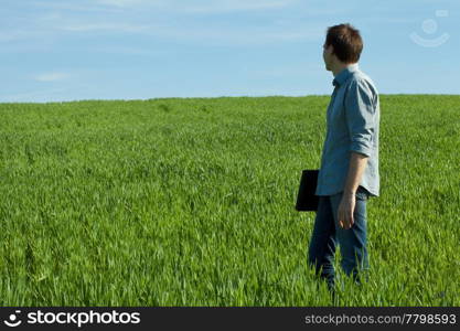 young man standing with a laptop in the green field