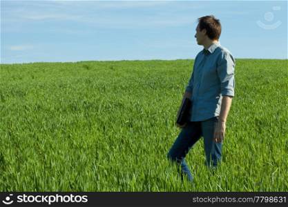 young man standing with a laptop in the green field