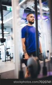 Young man standing with dumbbells at the gym. Working out. Indoor physical activity.. Young man standing with dumbbells at the gym