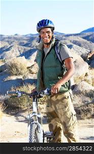 Young man standing with mountain bike in front of hills