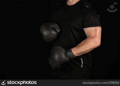 young man stands in a boxing rack, wearing very old vintage black boxing gloves on his hands, dark background